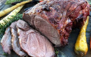 sliced leg of lamb surrouned by carrots and rosemary