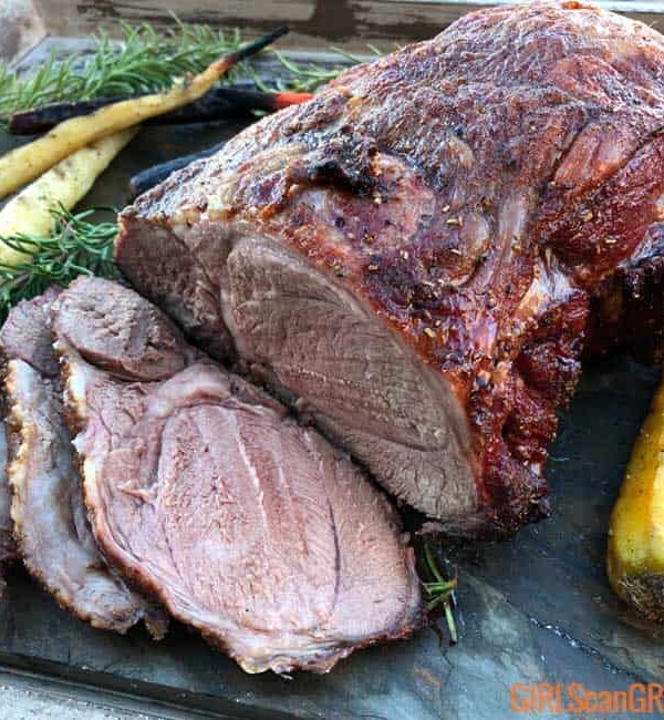 sliced leg of lamb surrouned by carrots and rosemary