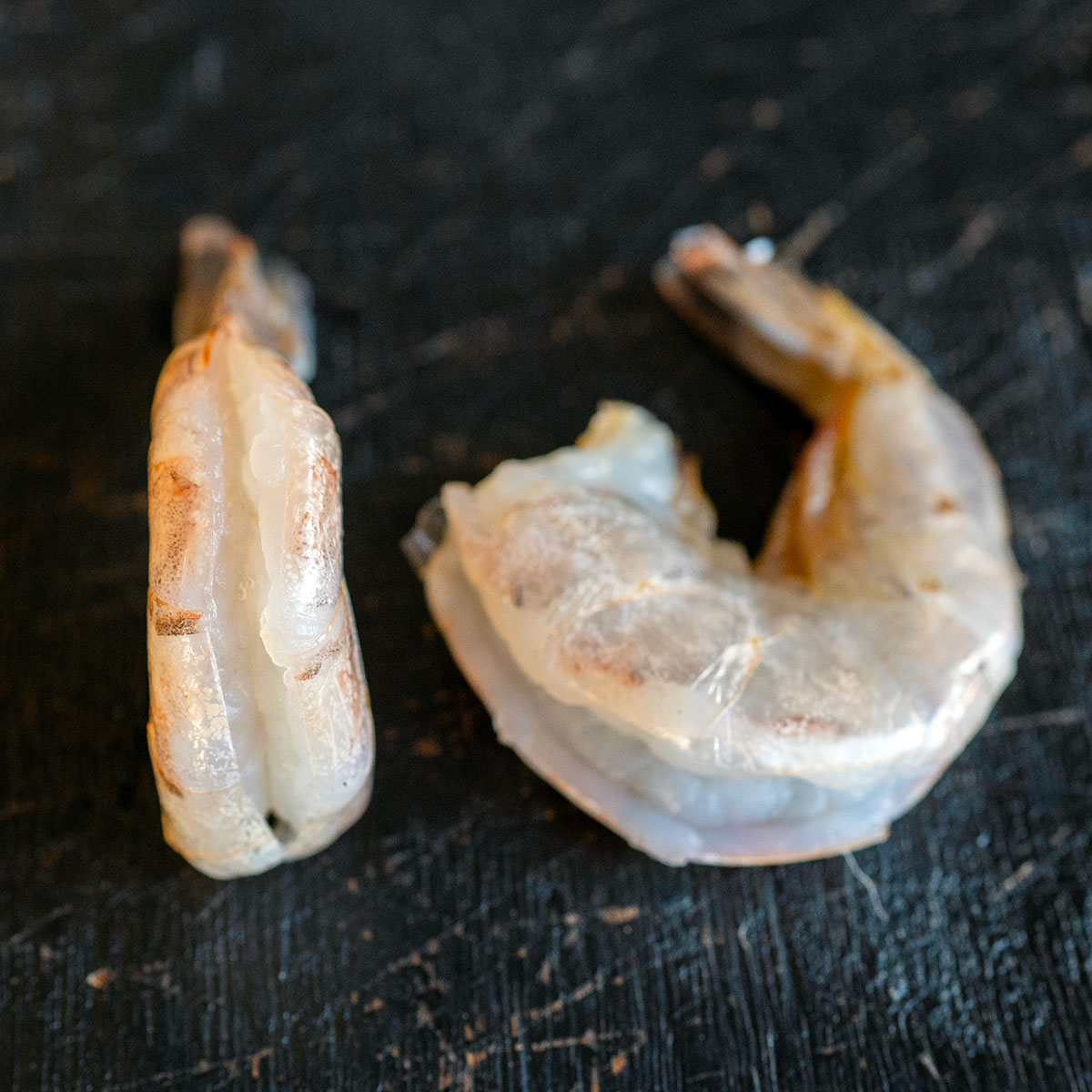 two pieces of shrimp, showing that they're deveined with the peel still on.