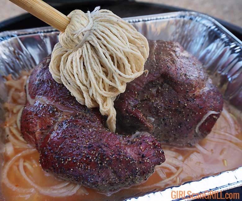 brushing a smoked lamb with a BBQ mop in a pan