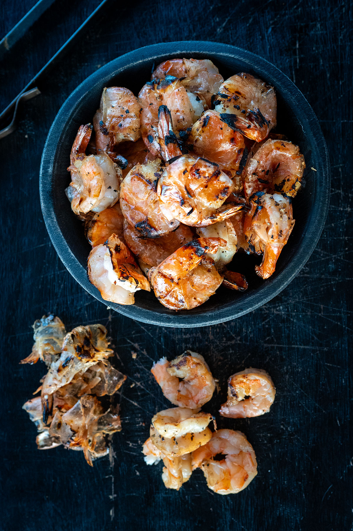 Bowl of grilled shrimp next to peeled shrimp and shrimp peels. 