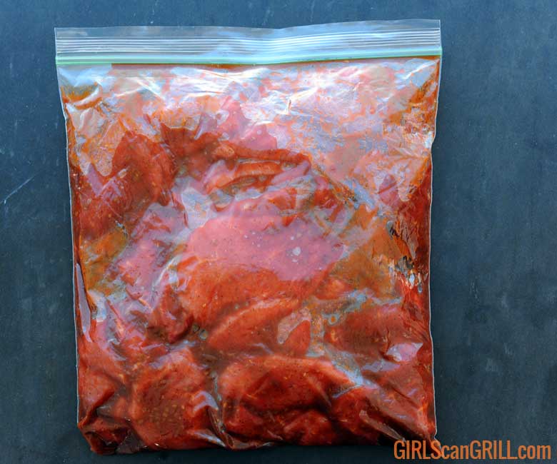 bag of sliced beef covered with red sauce on gray table