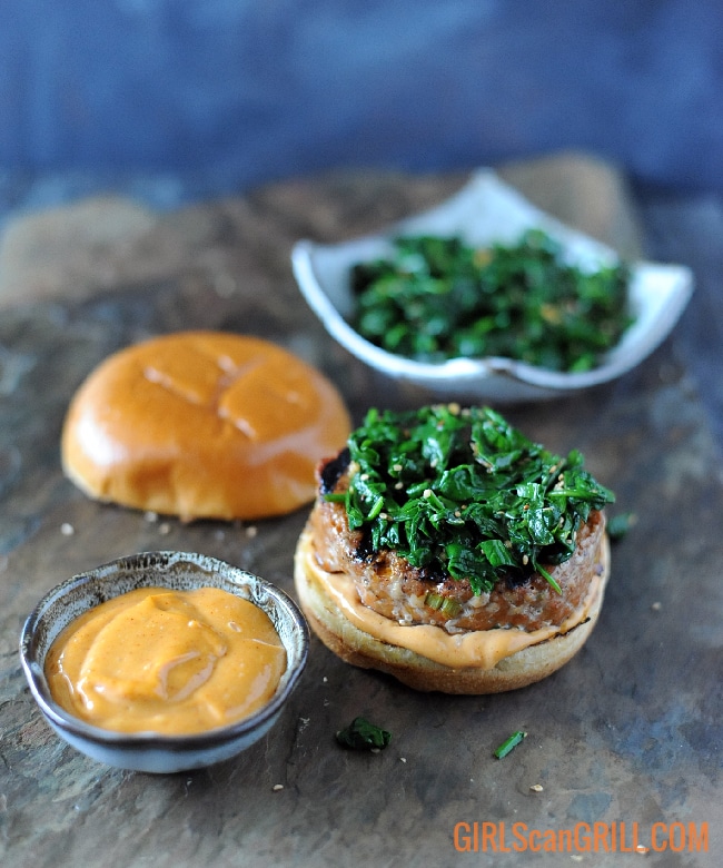 spinach on burger patty with bowl of spicy mayo in front and bowl of spinach toward back