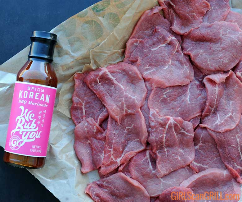 bottle of sauce with pink label next to sliced beef