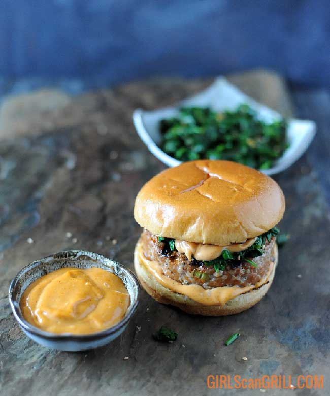 hamburger with bowl of spicy mayo in front and bowl of spinach toward back