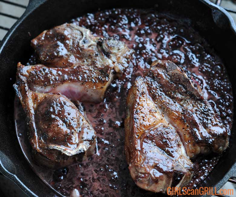 cast iron skillet with two lamb chops and cherry sauce
