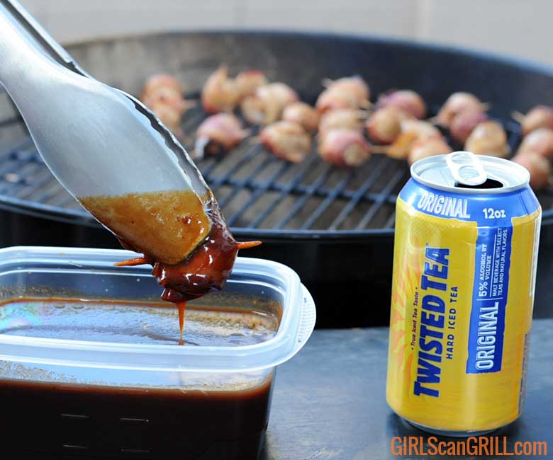 tongs dipping meatball in bbq sauce with grill in background and can of Twisted Tea to right