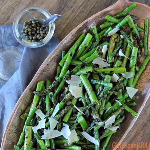 oval shaped copper dish with grilled asparagus inside with jar of capers in top left
