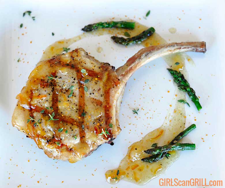 grilled pork chop on white plate with circle of glaze and asparagus