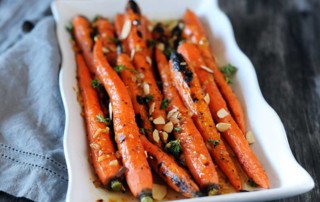 white plate with grilled whole carrots on gray board and napkin