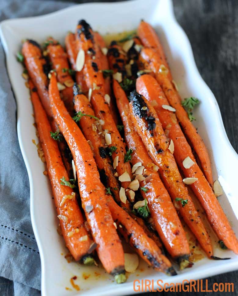 vertical white plate with grilled whole carrots on gray board and napkin