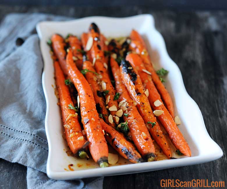 white plate with grilled whole carrots on gray board and napkin