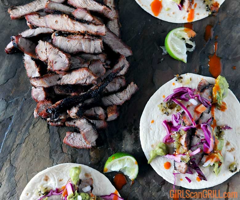 slate platter of sliced pork steak and three tacos with purple cabbage