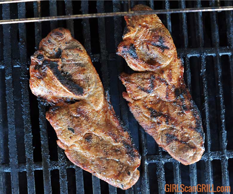 two pork steaks on a grill with char marks