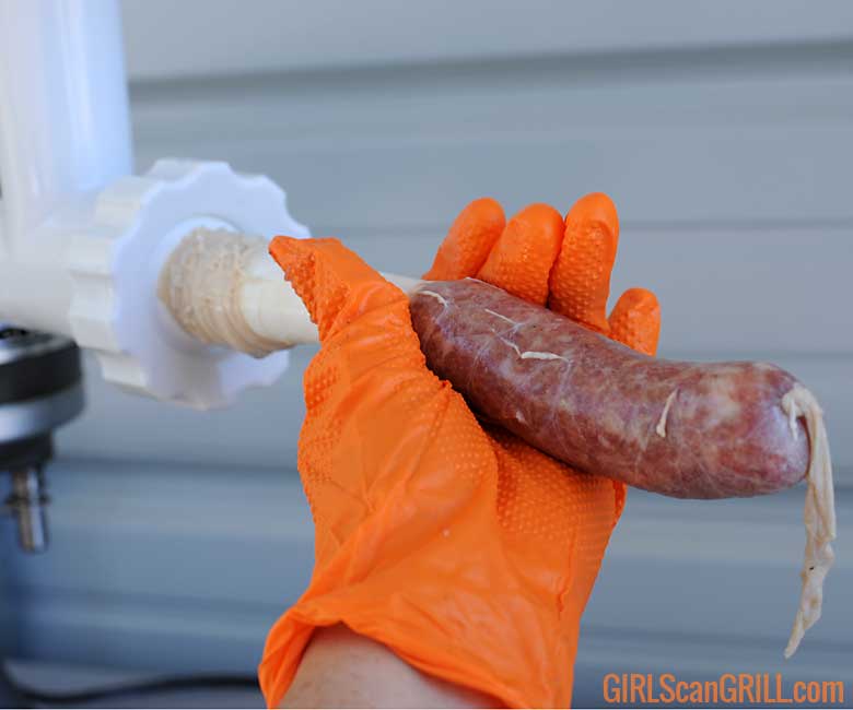 hand in orange glove holding sausage as it is being cased