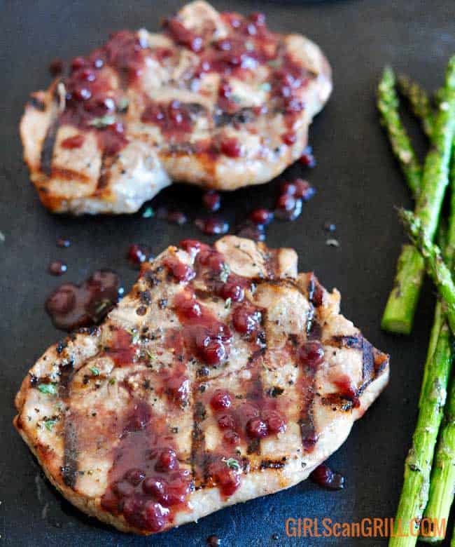 2 grilled pork porterhouse chops on a black background with a side of asparagus
