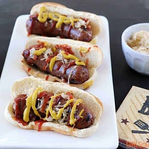 3 bratwurst on a white plate with mustard and ketchup