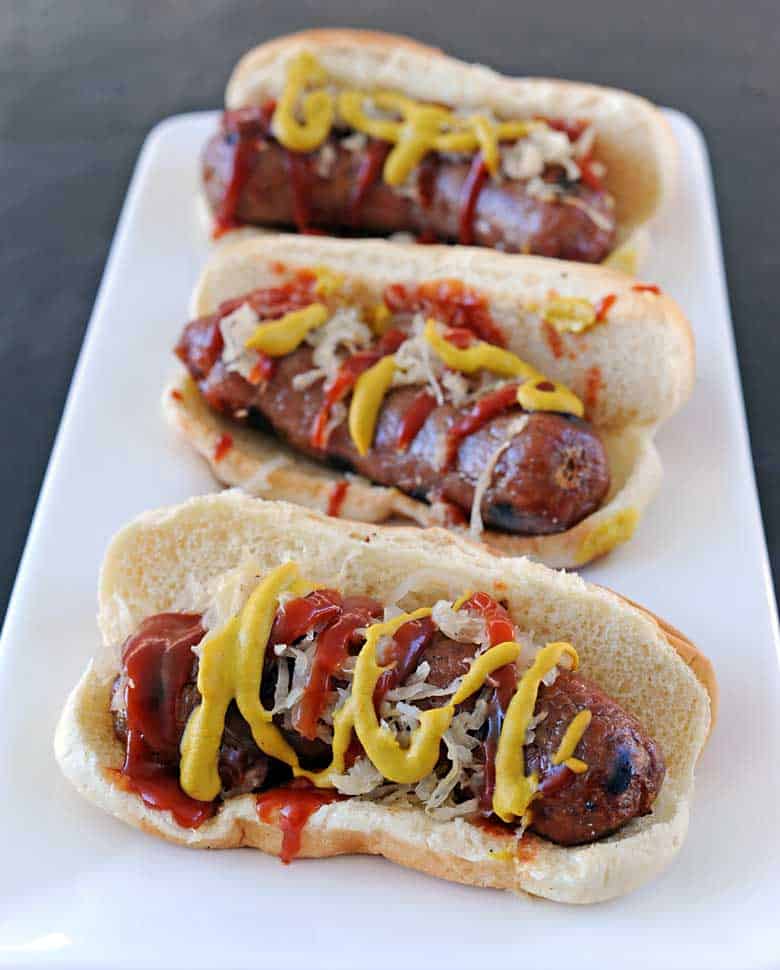3 bratwurst on a white plate with mustard and ketchup
