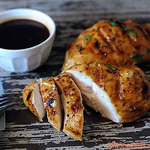 grilled sauced chicken breasts sliced on wooden platter with BBQ sauce in background