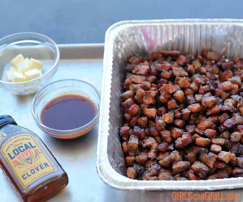 smoked pork belly cubes in aluminum pan next to bowls of butter, BBQ sauce and honey