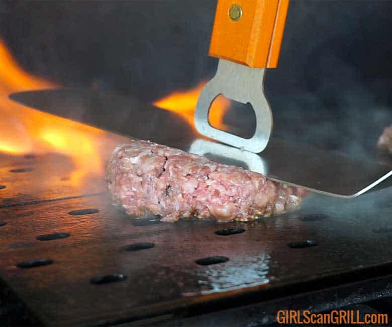 smashing burger on griddle with spatula with flames