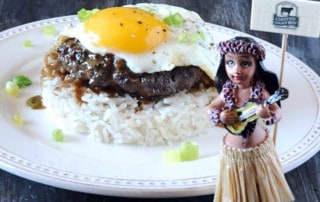 loco moco with egg on top of beef, gravy and rice with hula girl in front of plate