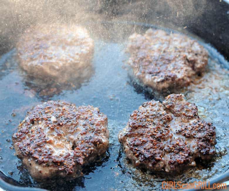 4 beef patties searing in cast iron skillet