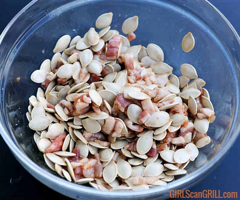 clear bowl full of pumpkin seeds, raw bacon and spices