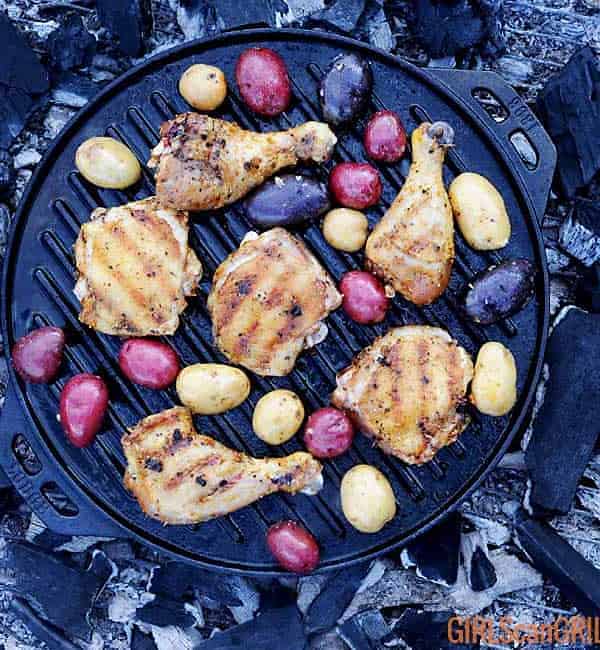 grilled chicken and potatoes in a cast iron pan over campfire