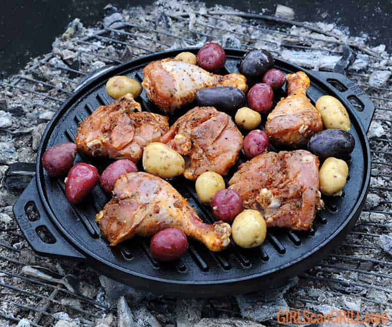 grilled chicken and potatoes in a cast iron pan over campfire