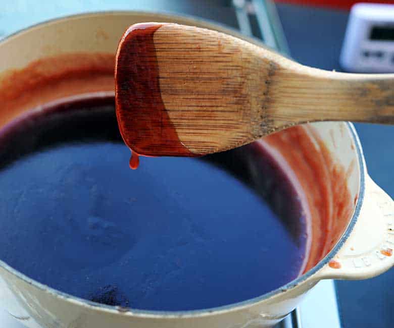 wooden spoon with drip of barbecue sauce coming off over pan.