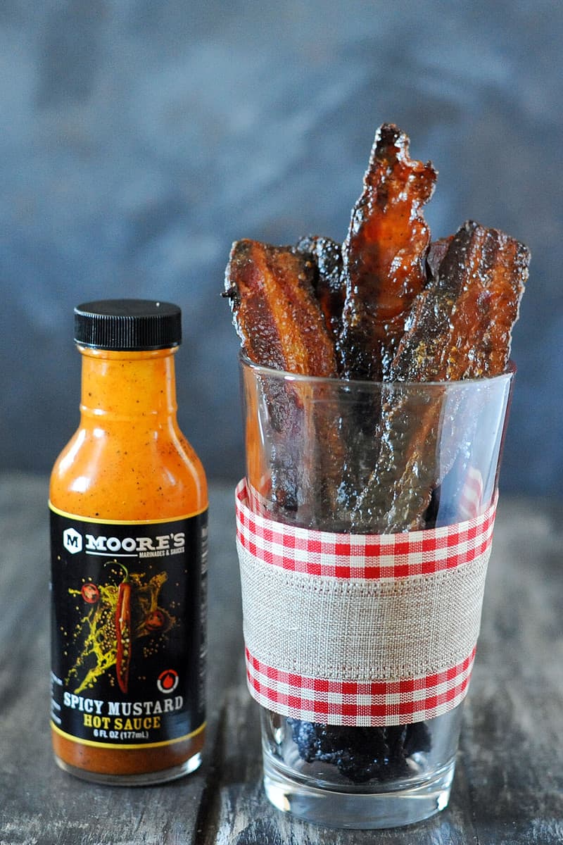 glass of cooked brown sugar bacon next to Moore's bottle of spicy mustard sauce.