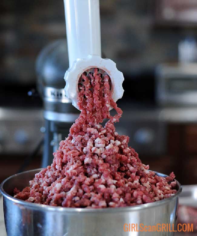 beef passing through a meat grinder into a metal bowl