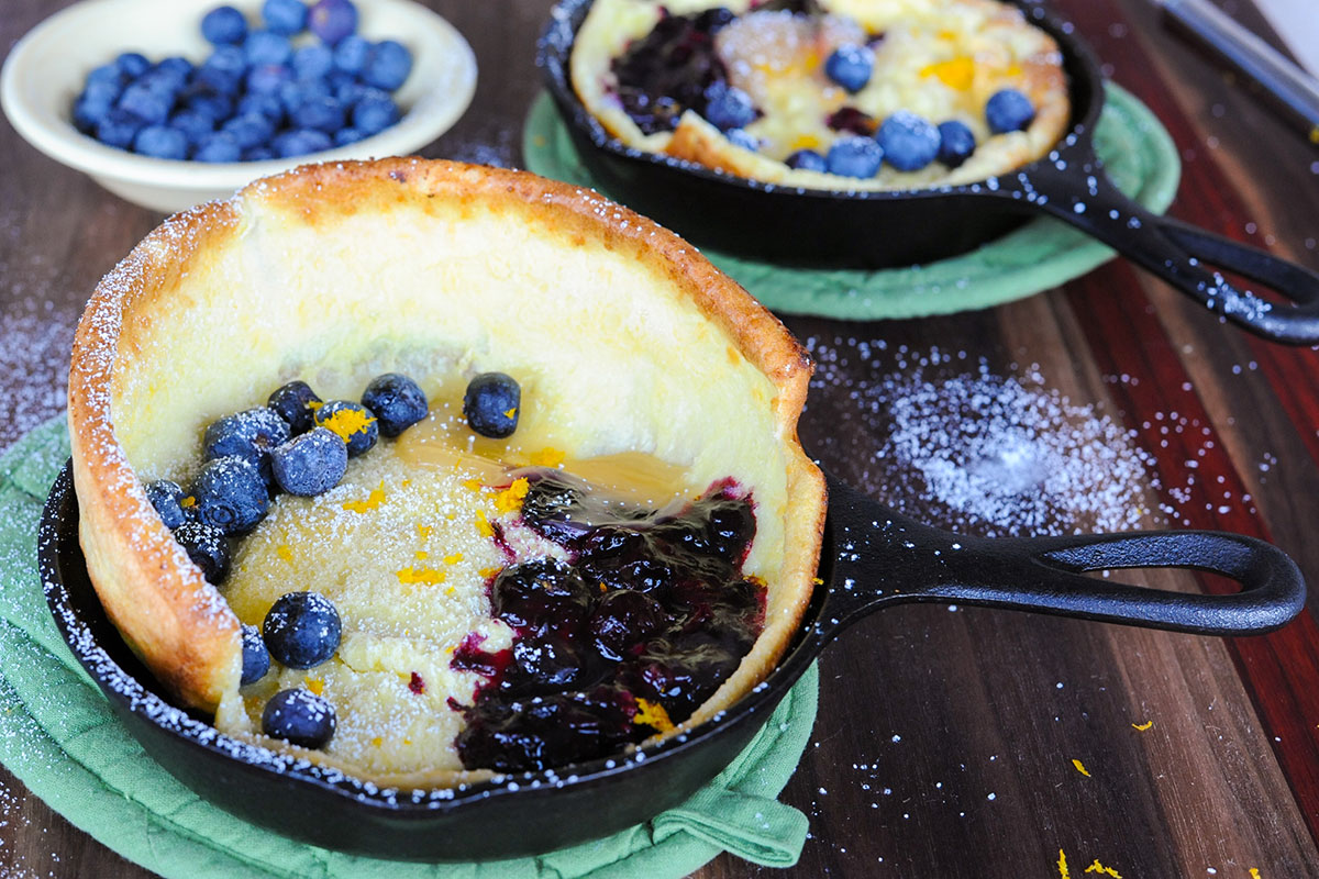 skillet with dutch baby pancake topped with blueberries and lemon curd.