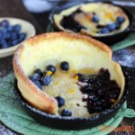 close up of dutch baby pancake with rise in skillet topped with blueberries