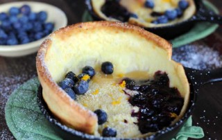 close up of dutch baby pancake with rise in skillet topped with blueberries