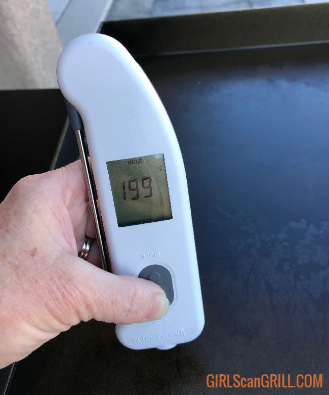 hand holding white thermometer above the griddle showing a temp of 199.