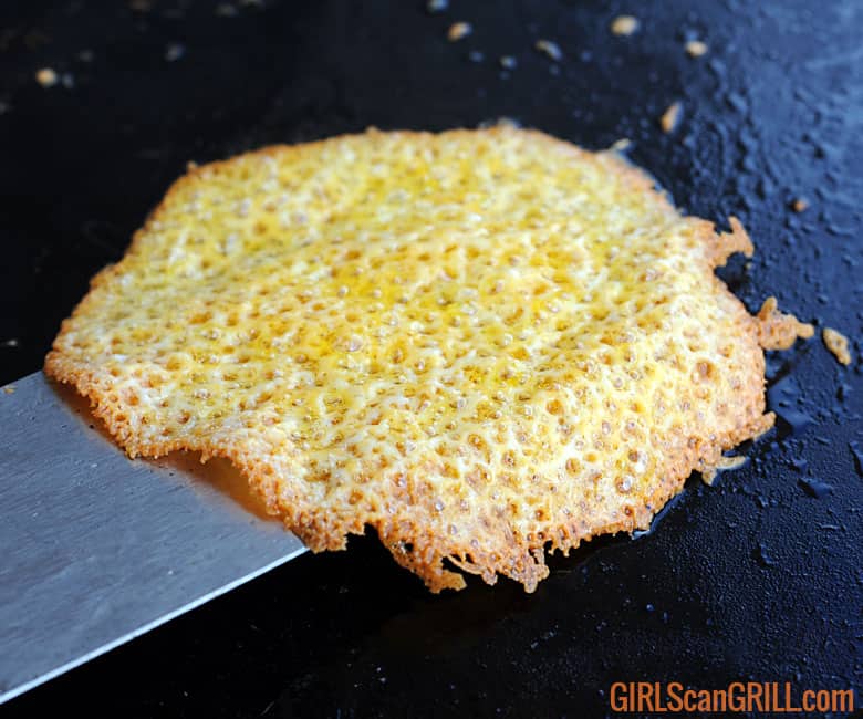 spatula scooping up cheese that has crisped up on a griddle