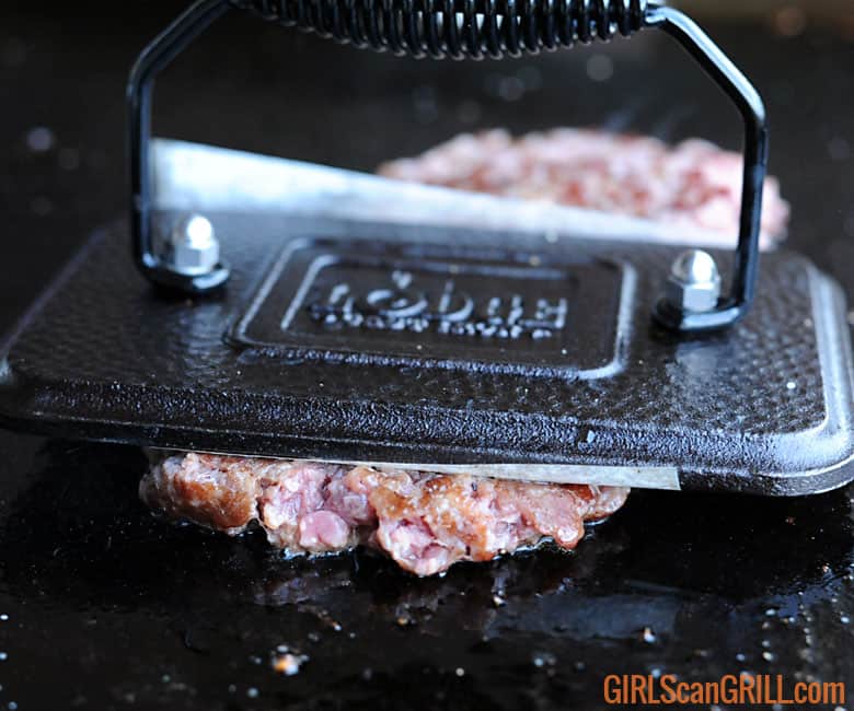 a bacon press smashes raw beef on a griddle