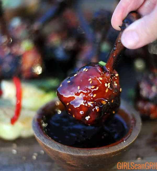 hand dunking Asian sticky chicken drumstick into a bowl of sauce