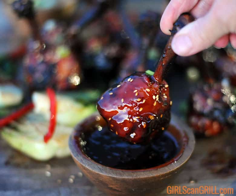 hand dunking Asian sticky chicken drumstick into a bowl of sauce