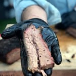 hand wearing black glove holding out a slice of brisket