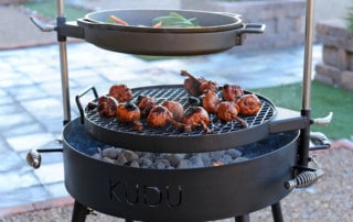 grate of chicken legs and skillet of bok choy searing above bed of coals on KUDU grill