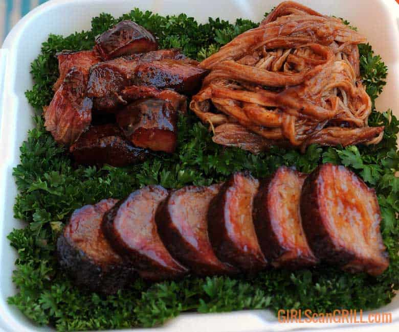 white box with bed of greens and three types of smoked pork