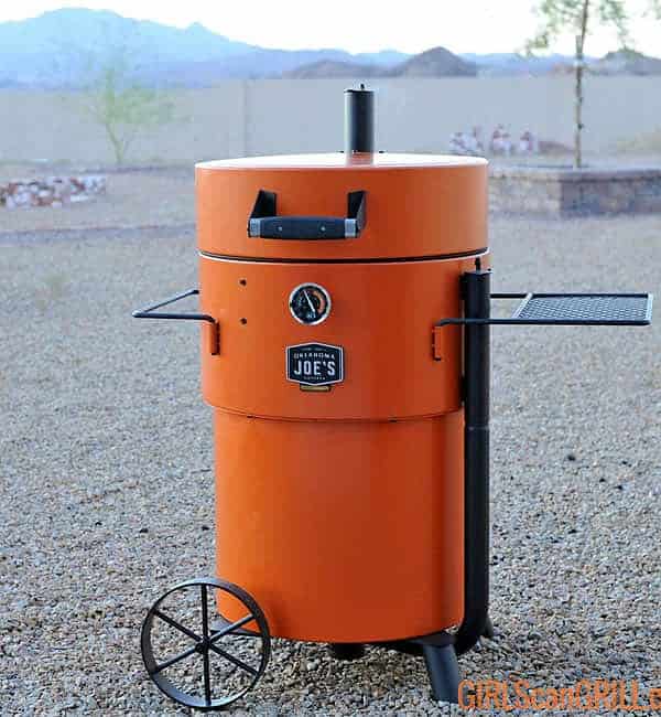 orange Oklahoma Joe's Bronco Pro Drum Smoker in rock backyard