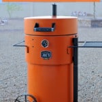 orange Oklahoma Joe's Bronco Pro Drum Smoker in rock backyard