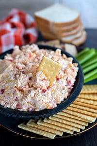 Bowl of pimento cheese with a cracker dipped inside.