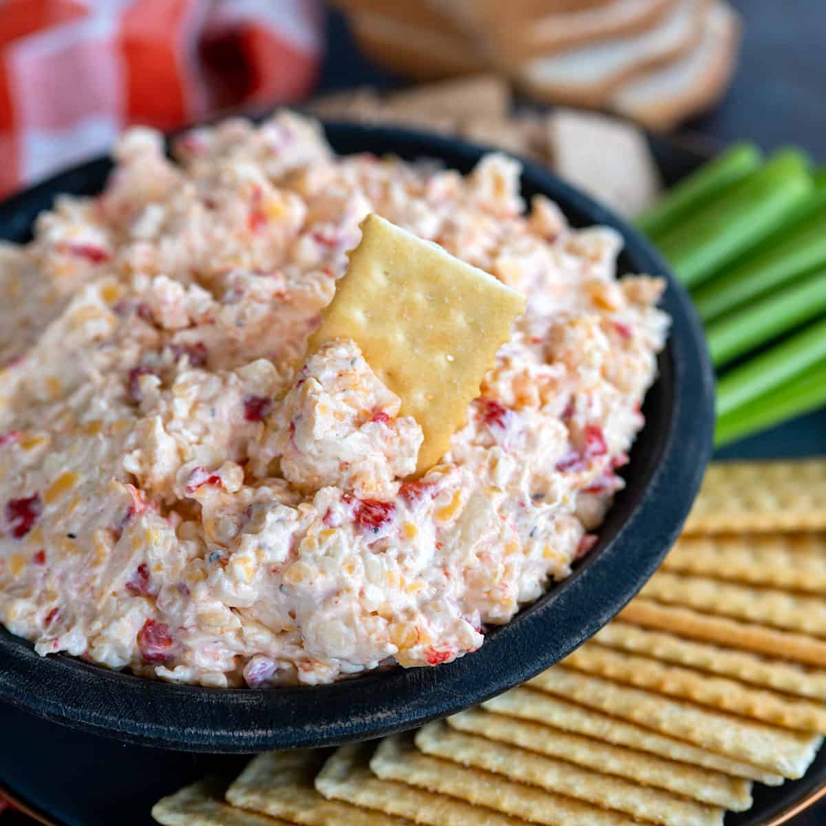 Bowl of pimento cheese with a cracker dipped inside.