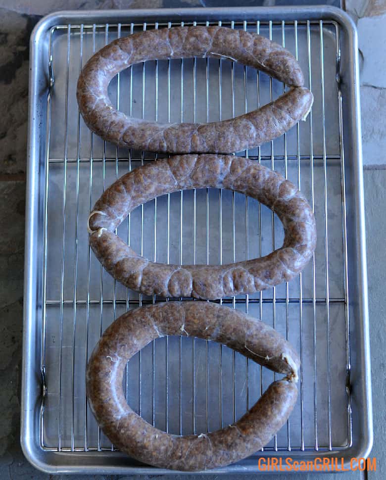 three beef sausage links cased, sitting on wire rack