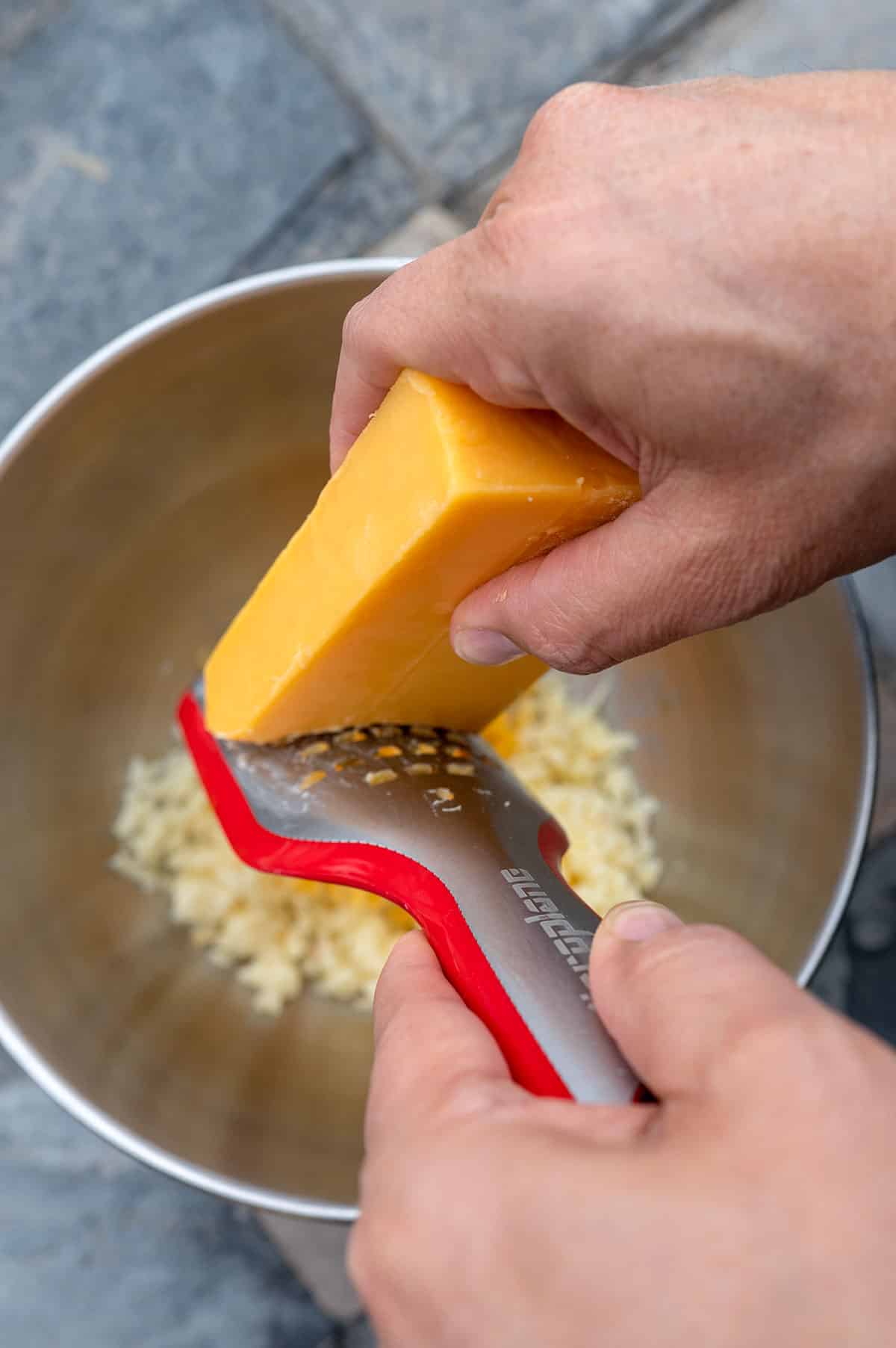 Shredding cheddar cheese into a bowl.